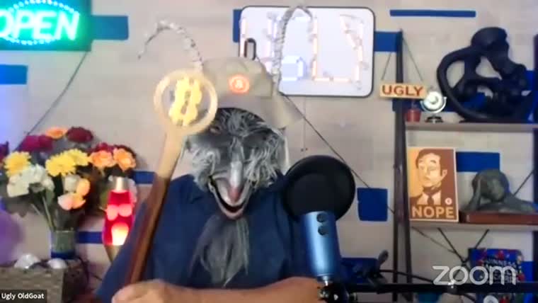 A man in a goat mask holds a staff topped with a golden Bitcoin disc in a home studio.