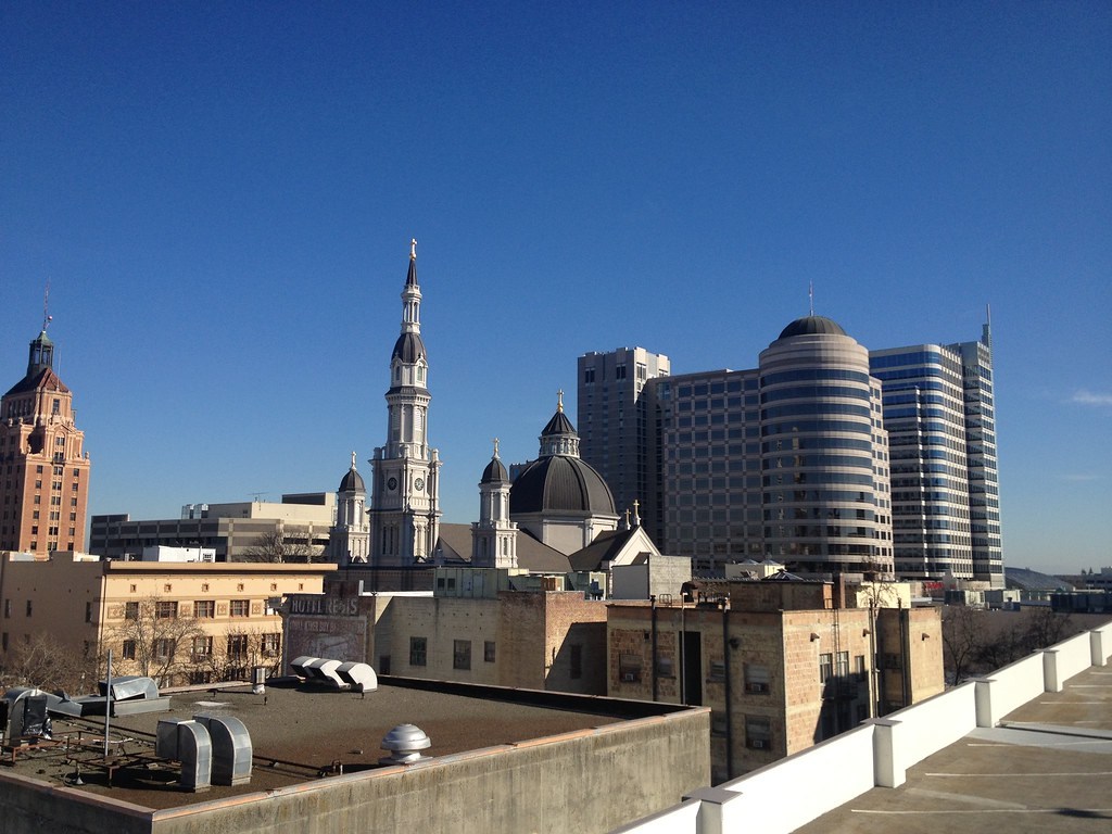 Sacramento rooftops and a church spire beneath a clear blue sky.