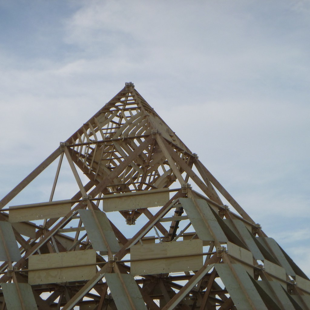 An upward view through a triangular structure of exposed wooden beams.