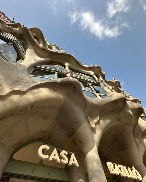 The curving facade of Casa Batlló, with its name visible, beneath a blue sky.