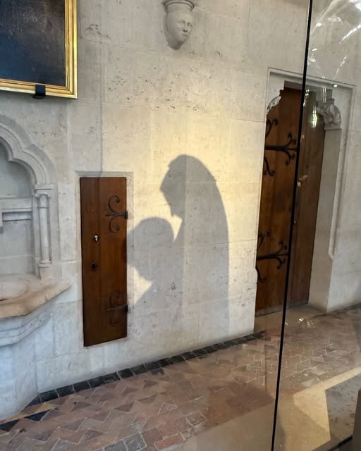 A long shadow falls across a pale interior wall beside a doorway and glass display.